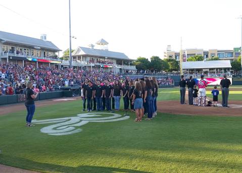 North Lamar High School Choir Director Rebecca Hildreth directs members of the Chamber Singers as they sing the national anthem before the first pitch of the Frisco Roughriders baseball game.